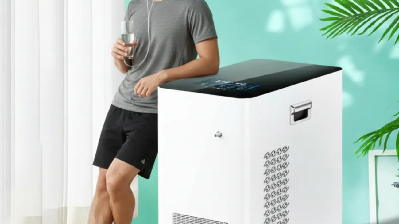 hydrogen oxygen ;A professional lifestyle photograph of a young man in athletic wear standing in a bright, modern room. He is leaning against a sleek, white medical-grade hydrogen inhalation machine with a digital touch display. He is wearing a nasal cannula connected to the device and holding a glass of clear water, looking calmly out of a window. A large green palm leaf and a minimalist side table with a hydrogen water bottle are in the background
